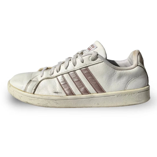 A single low-top sneaker shown in profile against a plain white background. The shoe appears to be a white leather sneaker with metallic rose-gold or copper-toned side stripes and matching laces.